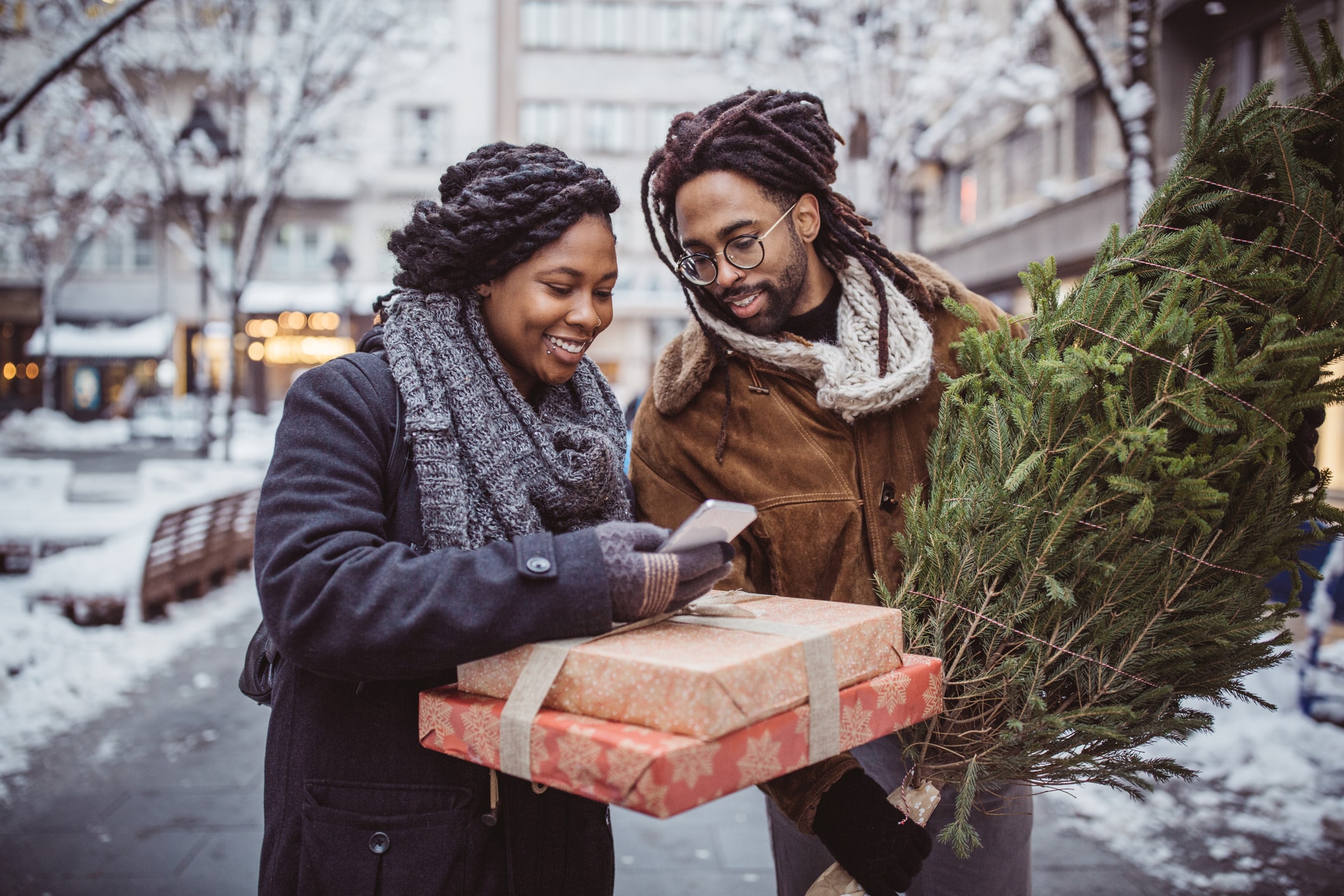 Young couple on Christmas market using mobile phone to find best retail holiday shopping